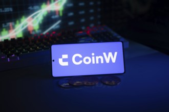 CoinW screen with coins, set in front of a neon-illuminated stock chart in blue