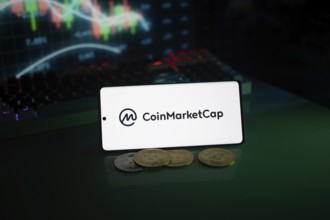 CoinMarketCap logo in a dark environment highlighted by coins and a glowing chart