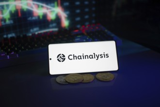 Chainalysis logo on phone, accompanied by coins and stock chart, highlighting digital finance