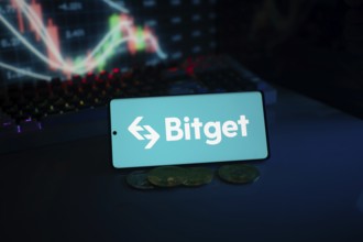 Bitget logo on smartphone with coins and stock chart, highlighting finance and trading theme