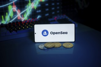 OpenSea logo on phone with coins and market chart, related to NFT and cryptocurrency