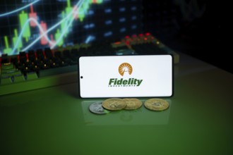 Phone displaying Fidelity Investments next to coins, with a financial market background