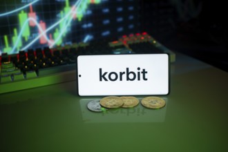 Mobile phone displaying Korbit near coins and market chart, suggesting cryptocurrency trading
