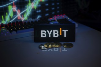 BYBIT logo on smartphone, accompanied by coins and stock chart, conveying trading theme
