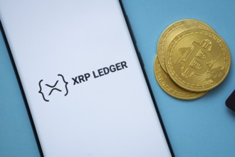 Dhaka, Bangladesh- 26 Aug 2025: XRP Ledger logo on smartphone screen near Bitcoin coin and QR code
