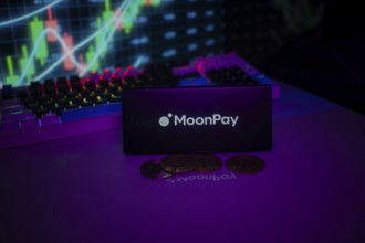 MoonPay logo on a purple screen with coins and trading graphs illuminated in the background