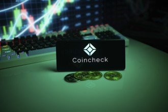 Coincheck on a smartphone with coins and stock market data in the background