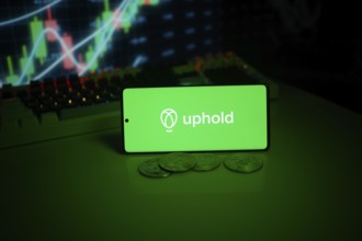 Uphold on a smartphone with coins and vivid stock market charts visible