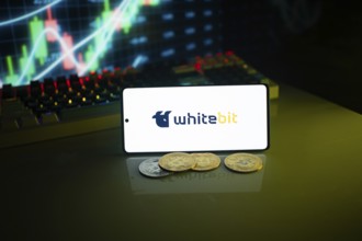 Whitebit displayed on a smartphone with coins and financial market visuals
