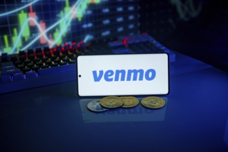 Phone displaying Venmo logo with coins and a backlit keyboard, signifying digital payments and
