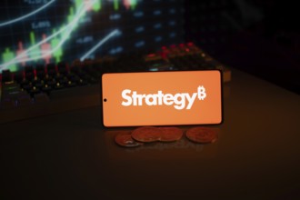 Phone shows Strategy logo with Bitcoin symbol and crypto coins on vivid screen