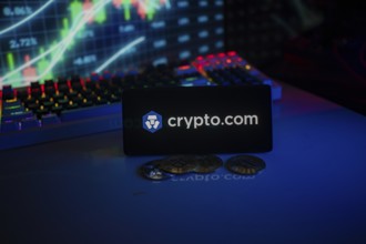 Phone displays Crypto.com logo with crypto coins and vibrant trading screen