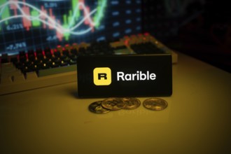 Phone displays Rarible logo with crypto coins and trading graph in background
