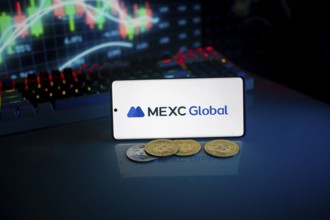 Phone shows MEXC Global logo with crypto coins and trading screen illuminated