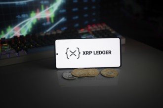 Phone displays XRP Ledger logo with crypto coins and trading graphics visible