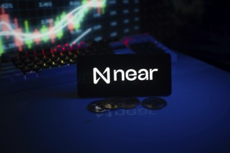 Near app on smartphone screen with coins and stock graph displayed behind