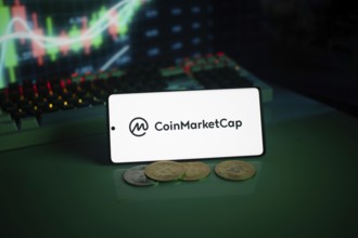 CoinMarketCap logo with coins and a glowing chart in a dim setting