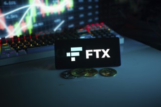 FTX logo on a screen in a dark setting with a glowing chart and coins