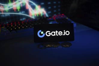 Gate.io logo displayed on a phone with cryptocurrency coins and market charts