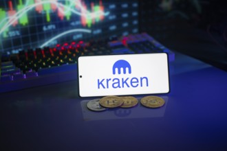 Kraken logo shown on a smartphone with digital currencies and trading charts behind
