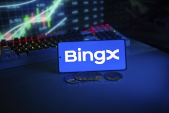 Bingx logo on a phone with digital currencies and financial charts in the background