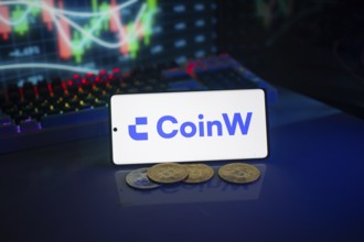 Coinw logo on a phone set against a backdrop of digital currencies and trading charts