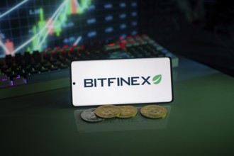 Bitfinex logo on a smartphone with cryptocurrencies and financial trading graphs behind