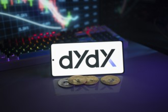 Dydx logo displayed on a phone with digital currencies and trading charts in the background