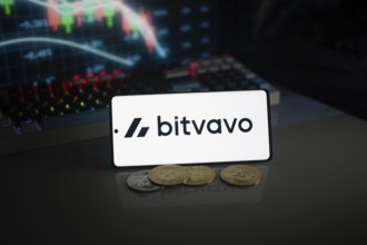 Bitvavo logo on smartphone with coins, neon lights, and trading charts in background