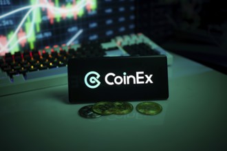 CoinEx logo displayed with coins on a desk and trading graphs in the background