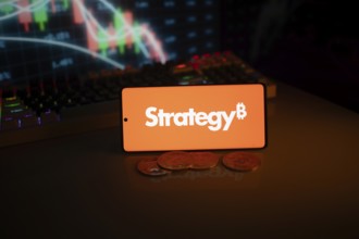 Phone shows Strategy logo with Bitcoin symbol and crypto coins on vivid screen