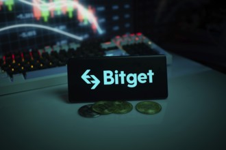 Bitget logo with coins on a desk, set against trading graphs backdrop