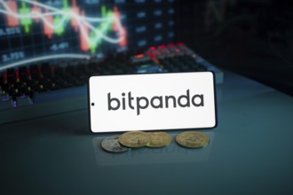 Bitpanda logo on white screen with coins and trading graphs in the background