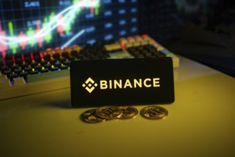 Binance logo on black screen with coins and trading graphs in background