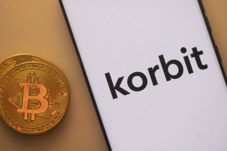 Korbit logo displayed on a smartphone with a Bitcoin on an orange backdrop