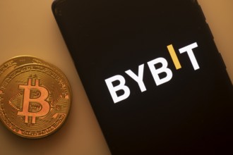 Bybit logo on a black smartphone beside a Bitcoin on an orange background