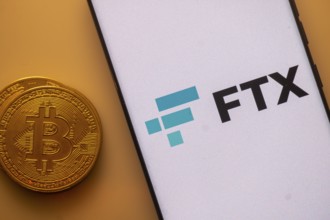 FTX logo displayed on a phone beside a Bitcoin on an orange background
