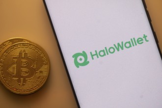 Smartphone displaying HaloWallet logo beside a physical Bitcoin on an orange background