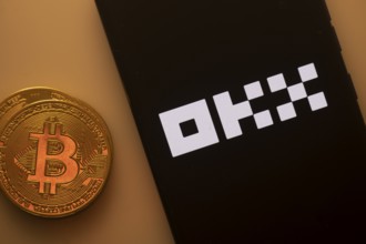 Bitcoin coin next to a smartphone featuring the OKX logo on a dark background