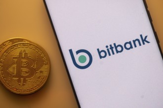 Smartphone featuring Bitbank logo alongside a Bitcoin on an orange background