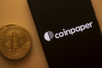Bitcoin next to smartphone displaying Coinpaper app on a black background