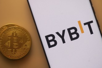 Bitcoin near a smartphone featuring the Bybit logo under orange lighting
