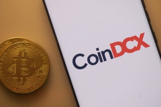 Bitcoin coin besides CoinDCX logo on a smartphone, illuminated by an orange hue