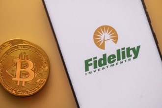 Bitcoin coin next to a smartphone displaying the Fidelity Investments logo on a light background