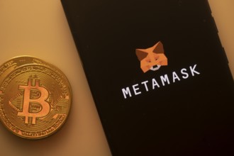 Bitcoin coin near a smartphone with the MetaMask logo on a dark background