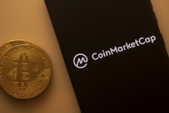 Bitcoin coin beside a phone showing the CoinMarketCap logo on a black screen