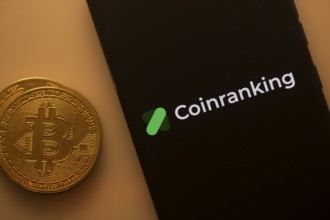 Bitcoin coin beside a phone displaying the Coinranking logo on a black screen