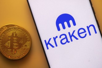 Bitcoin coin next to a smartphone with the Kraken logo on a white screen