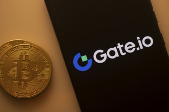 Bitcoin coin adjacent to a phone with the Gate.io logo on a black screen