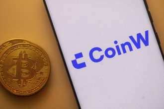 CoinW app shown on a smartphone next to a Bitcoin coin